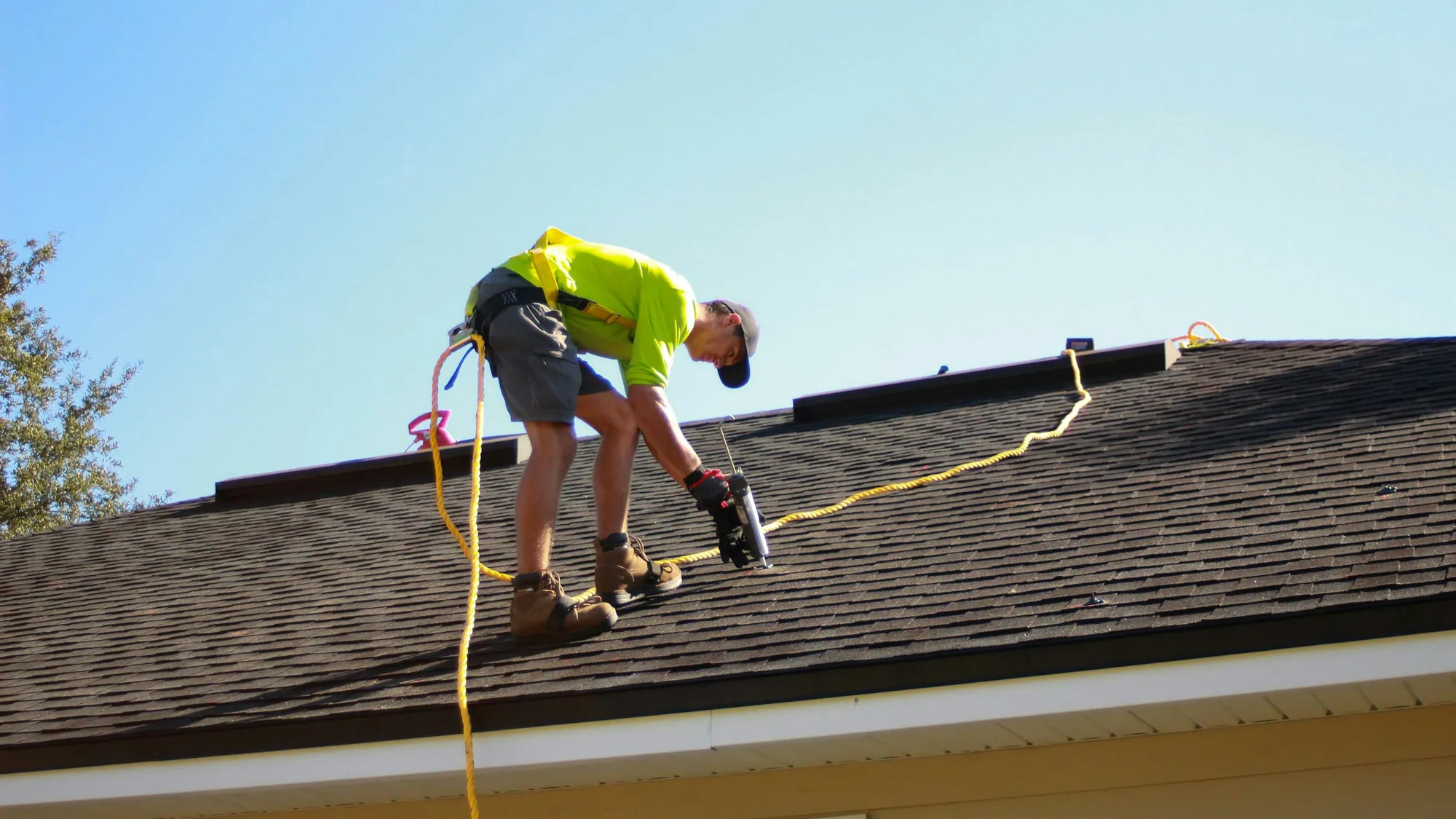 Roofer nailing shingles on a house roof under a clear sky